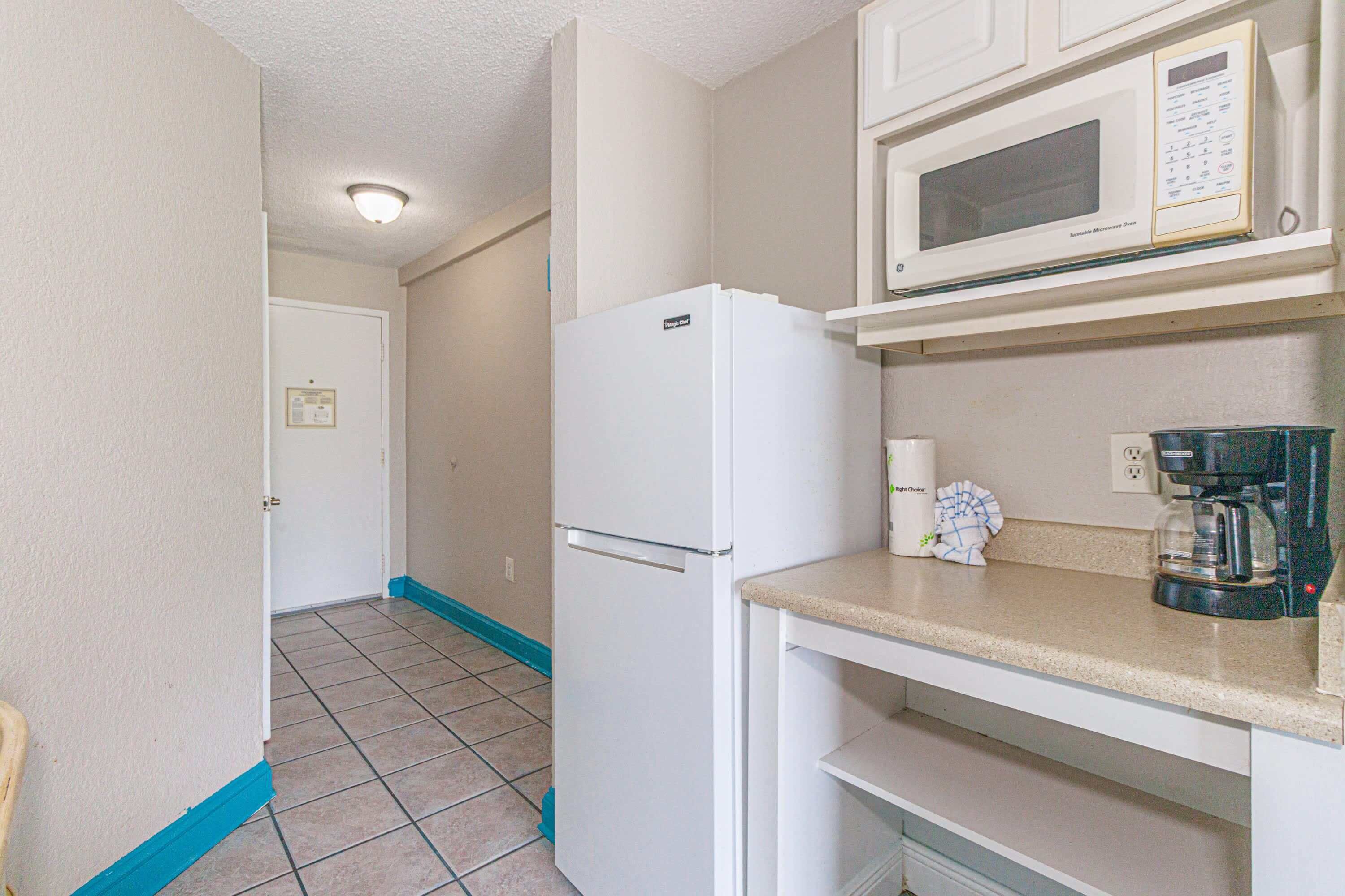 A compact kitchenette with a white refrigerator, a microwave, and a coffee maker on the countertop.