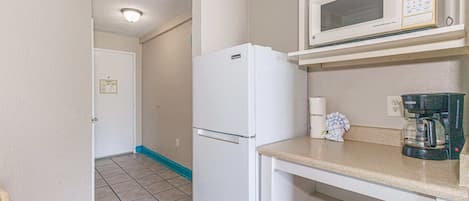 A compact kitchenette with a white refrigerator, a microwave, and a coffee maker on the countertop.