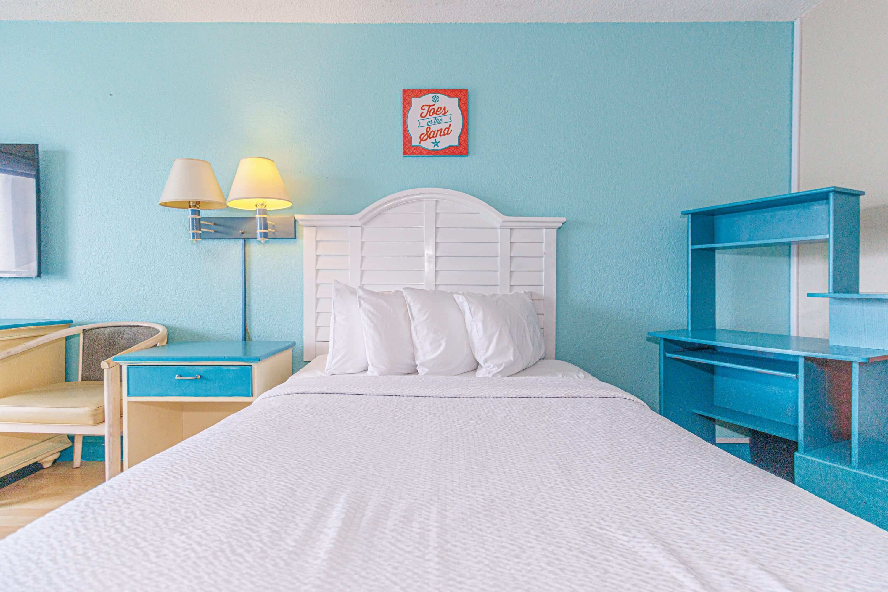 A bedroom with a bed, bedside lamps, a desk, and a chair.