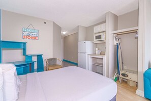 Une petite pièce, de taille modeste, comprenant un lit, un bureau, une chaise, un four à micro-ondes et un réfrigérateur.