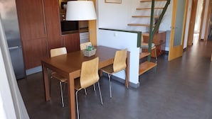 Et moderne køkken med træskabe, et spisebord med stole, en trappe med grønt gelænder og en vægmonteret lampe.