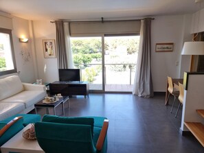 A modern living room with a sofa, a television, and a dining area with chairs. - Apartment with AC, terrace - 6 guests (L'Escala)
