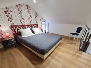 Un dormitorio con una cama de madera, una mesita de noche con lámpara, una silla y una escalera.