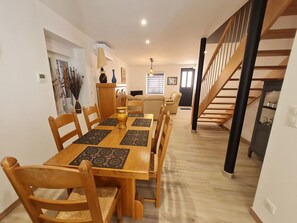 Un coin repas avec une table et des chaises en bois, une cuisine à l’arrière-plan et un escalier.