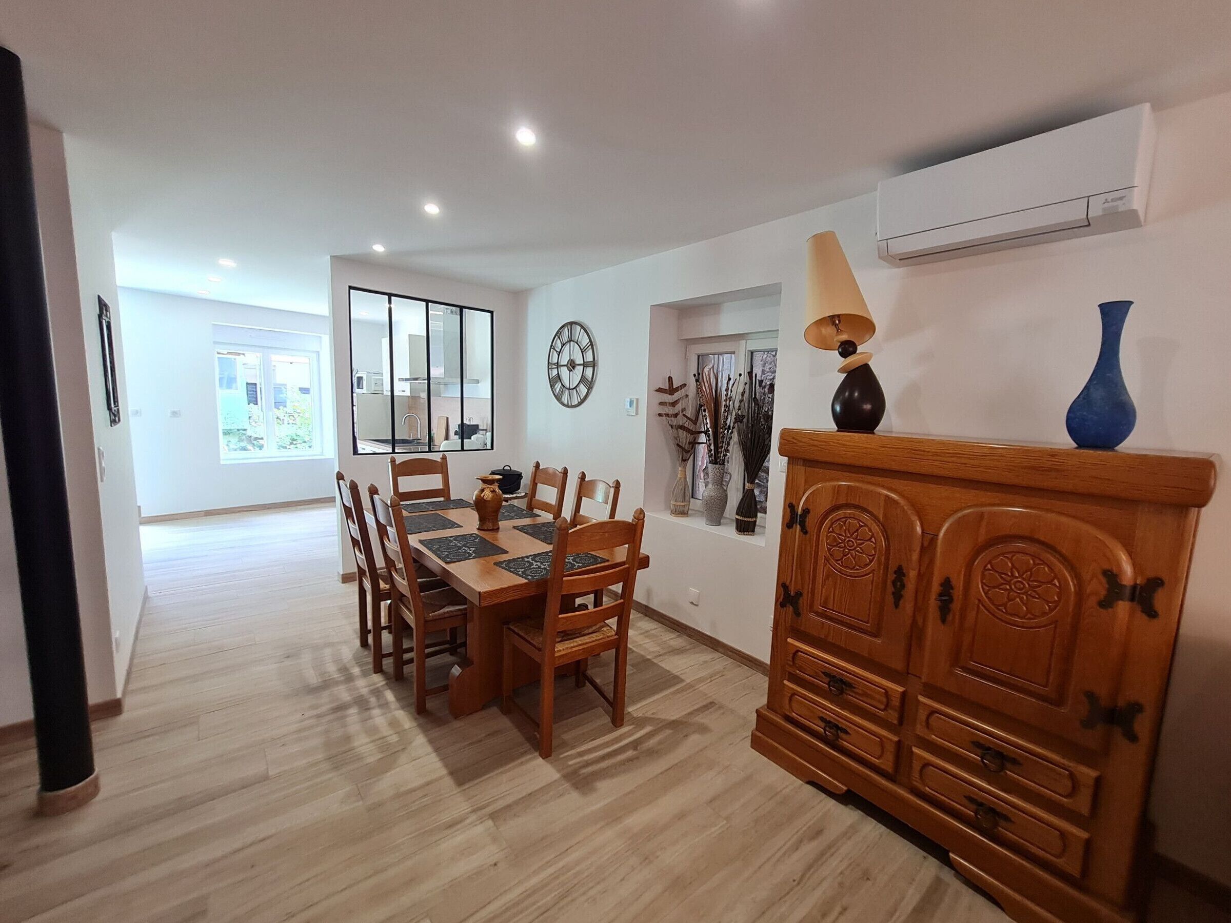A dining area with a wooden table and chairs, a decorative cabinet, and a wall-mounted clock.