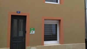 Rakennuksessa on musta ovi, valkoinen ikkunaluukku ja vihreä kyltti, jossa lukee »GITE» ja »GITE DE FRANCE».