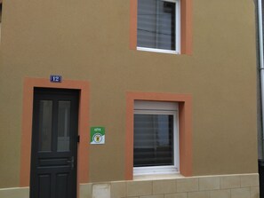 Un bâtiment avec une porte noire, une fenêtre avec un store blanc et une enseigne verte sur le mur, portant les inscriptions « GITE » et « GITE DE FRANCE ».