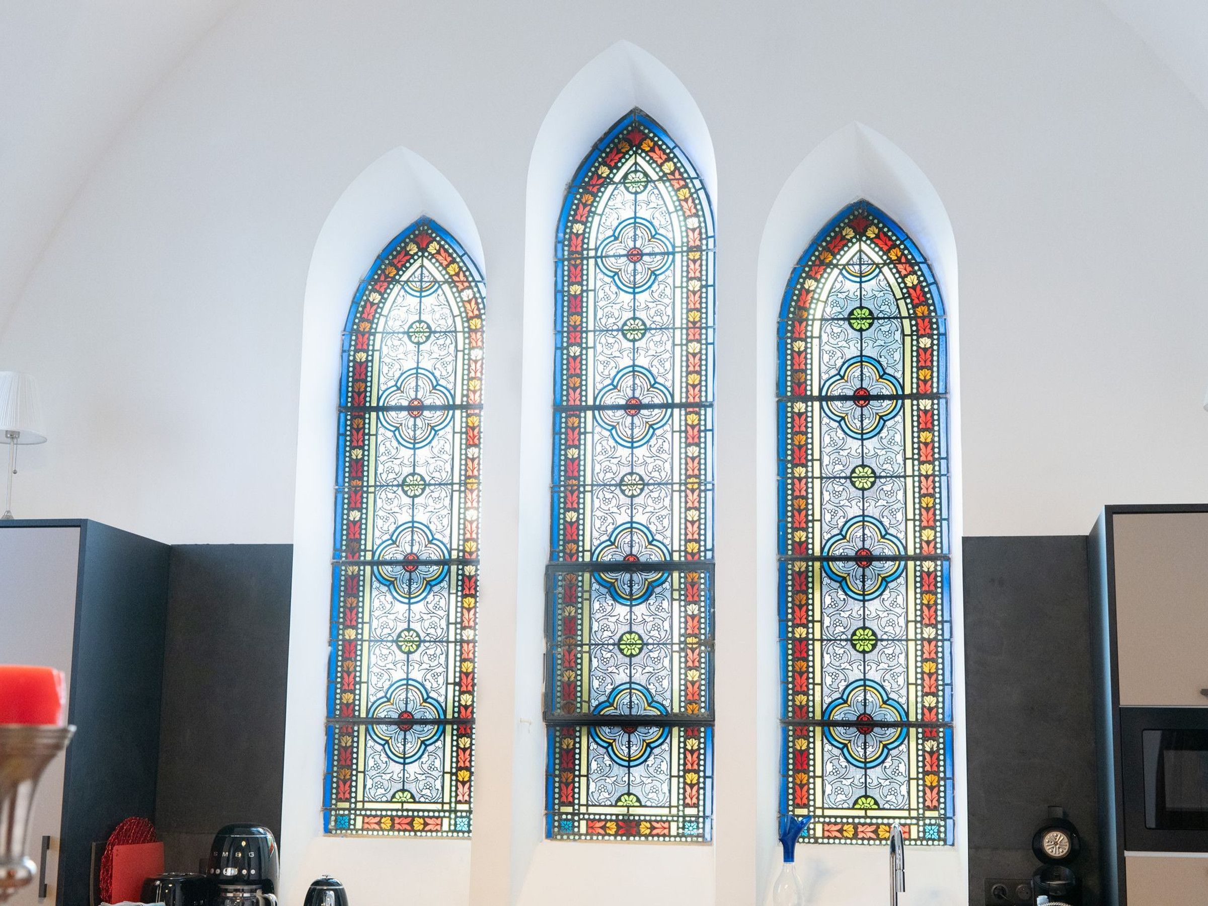 A room with three tall, narrow windows featuring intricate stained glass designs.