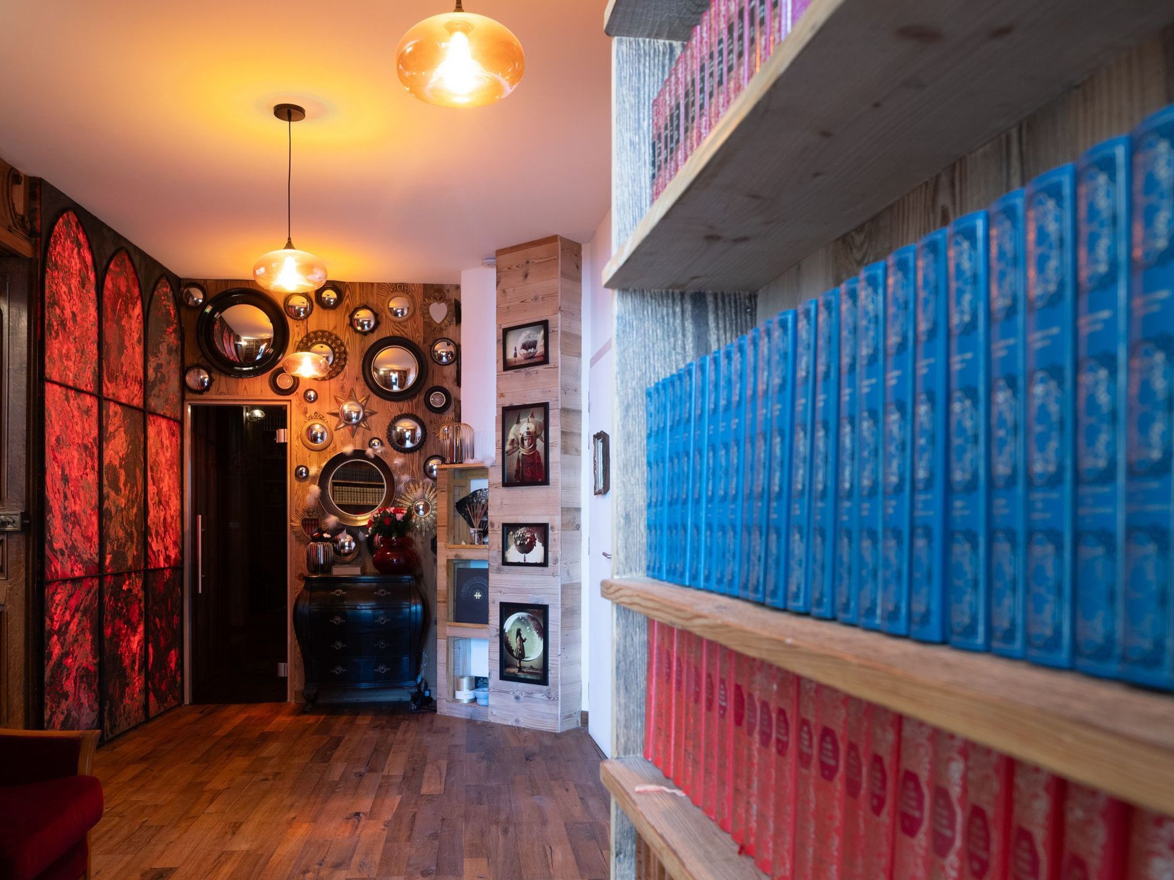 Een gang met een houten vloer, een zwarte dressoir en een muur versierd met spiegels en ingekaderde foto's.