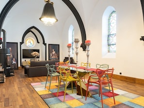 A dining area with a wooden floor, colorful chairs, a table with a red tablecloth, and a chandelier.