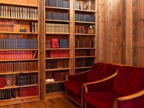 Une bibliothèque avec des étagères en bois remplies de livres, un fauteuil en velours rouge et un plancher en bois.