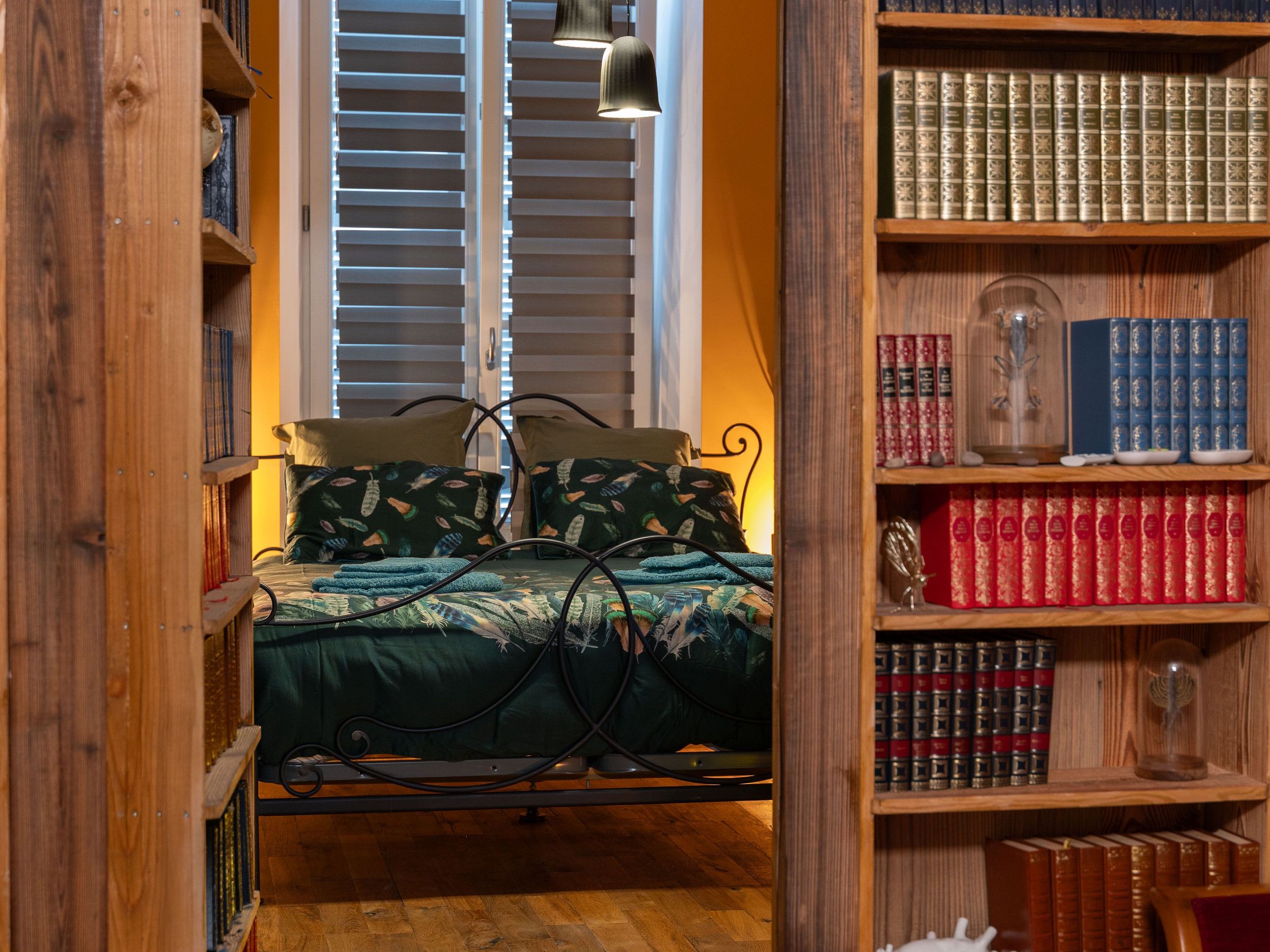 Een slaapkamer met een bed, een boekenkast en een raam met jaloezieën.