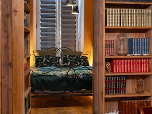 A bedroom with a bed, a bookshelf, and a window with blinds.