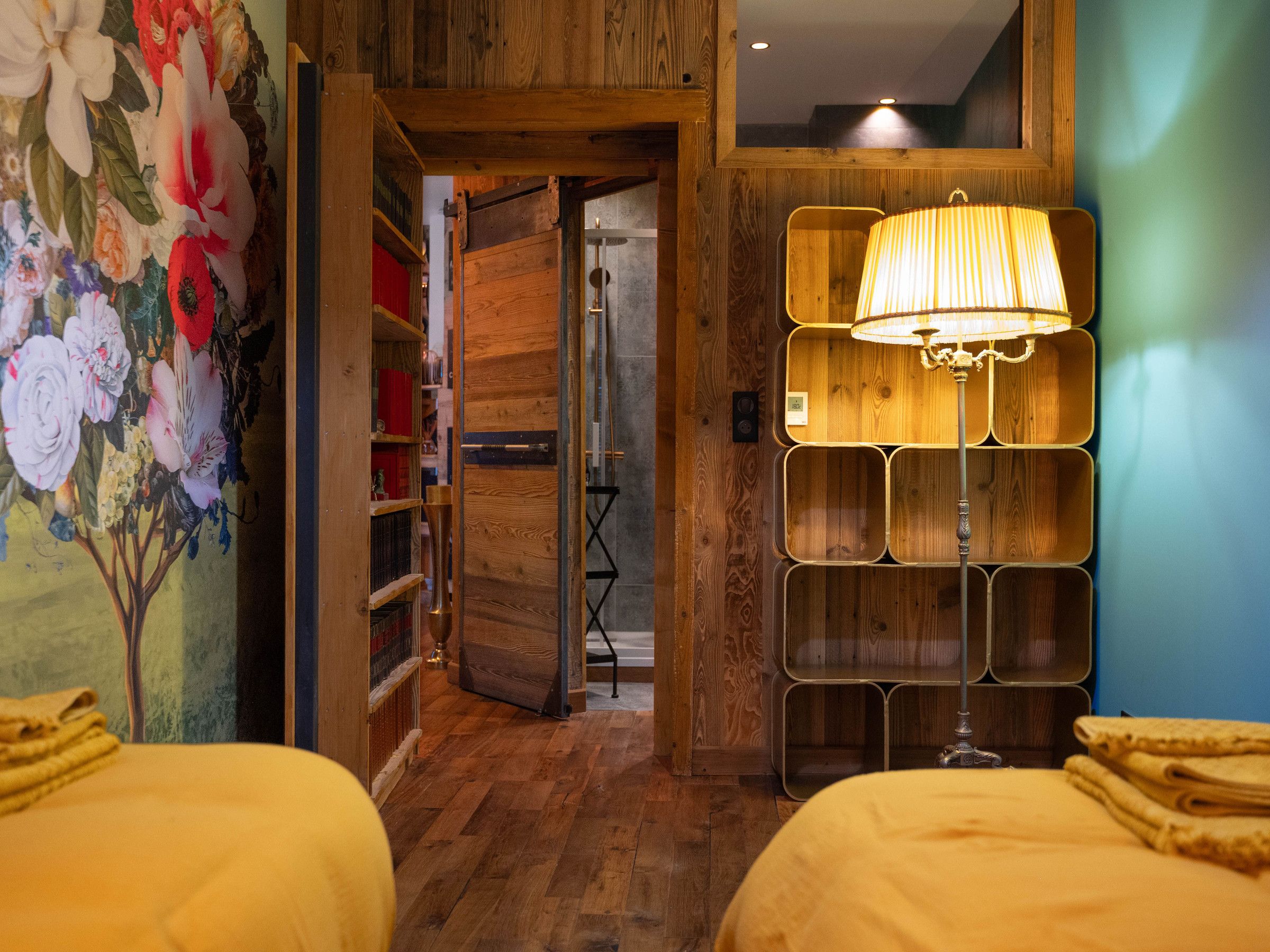 Ein Zimmer mit Holzboden, einer Wandmalerei mit Blumenmuster, einem Bett mit gelber Bettwäsche und einer einzigartigen Wandleuchte.