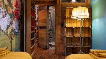 Ein Zimmer mit Holzboden, einer Wandmalerei mit Blumenmuster, einem Bett mit gelber Bettwäsche und einer einzigartigen Wandleuchte.