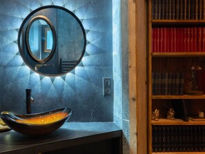 Un baño con un espejo redondo, un lavabo y una repisa con libros y objetos decorativos.