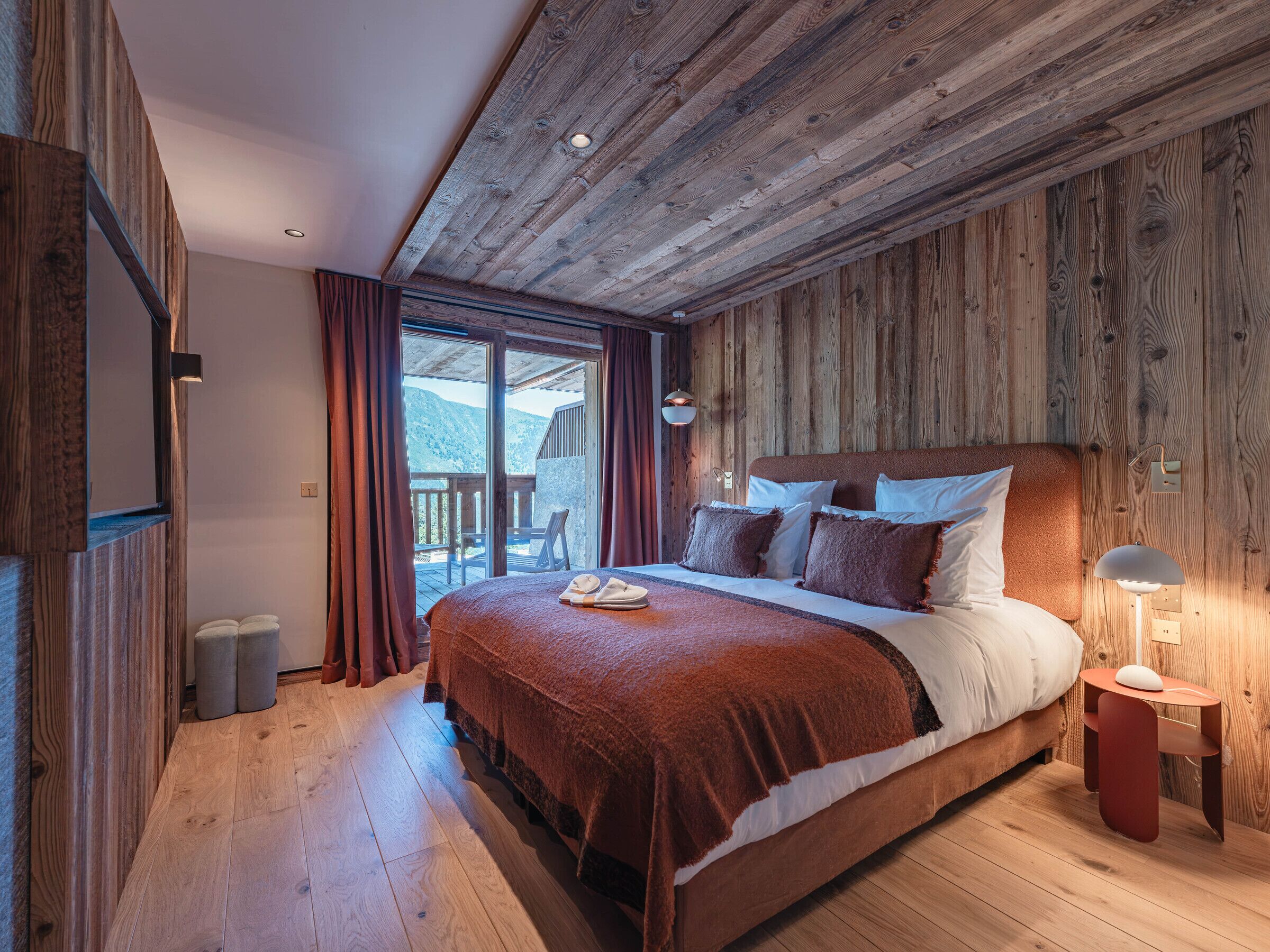 A wooden-paneled bedroom with a large bed, a nightstand, and a view of the outdoors.