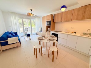 A modern kitchen with white cabinets, a dining table set for four, and a blue sofa in the living area. - Apartment with AC and parking - 4 guests (Le Lavandou)