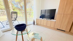 Una sala de estar moderna con una mesa de vidrio, un tazón azul, un televisor sobre un mueble de madera y vistas a un balcón.