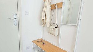 Habitación blanca con un banco de madera, un espejo, una puerta con picaporte y un bolso colgado.
