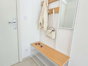 Ein heller Raum mit einer Holzbank, einem Spiegel, einer Tür mit Griff und einer aufhängbaren Tasche.