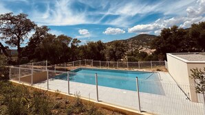 Una piscina rectangular con valla blanca, rodeada de árboles y colinas al fondo.
