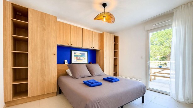 Un dormitorio con una cama, pared azul, armario de madera y vistas al exterior.