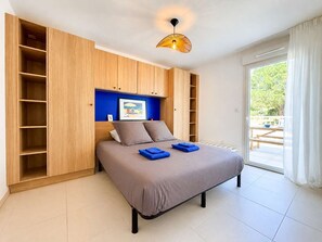A bedroom with a bed, a blue wall, a wooden wardrobe, and a view to the outside. - Apartment with AC and parking - 4 guests (Le Lavandou)