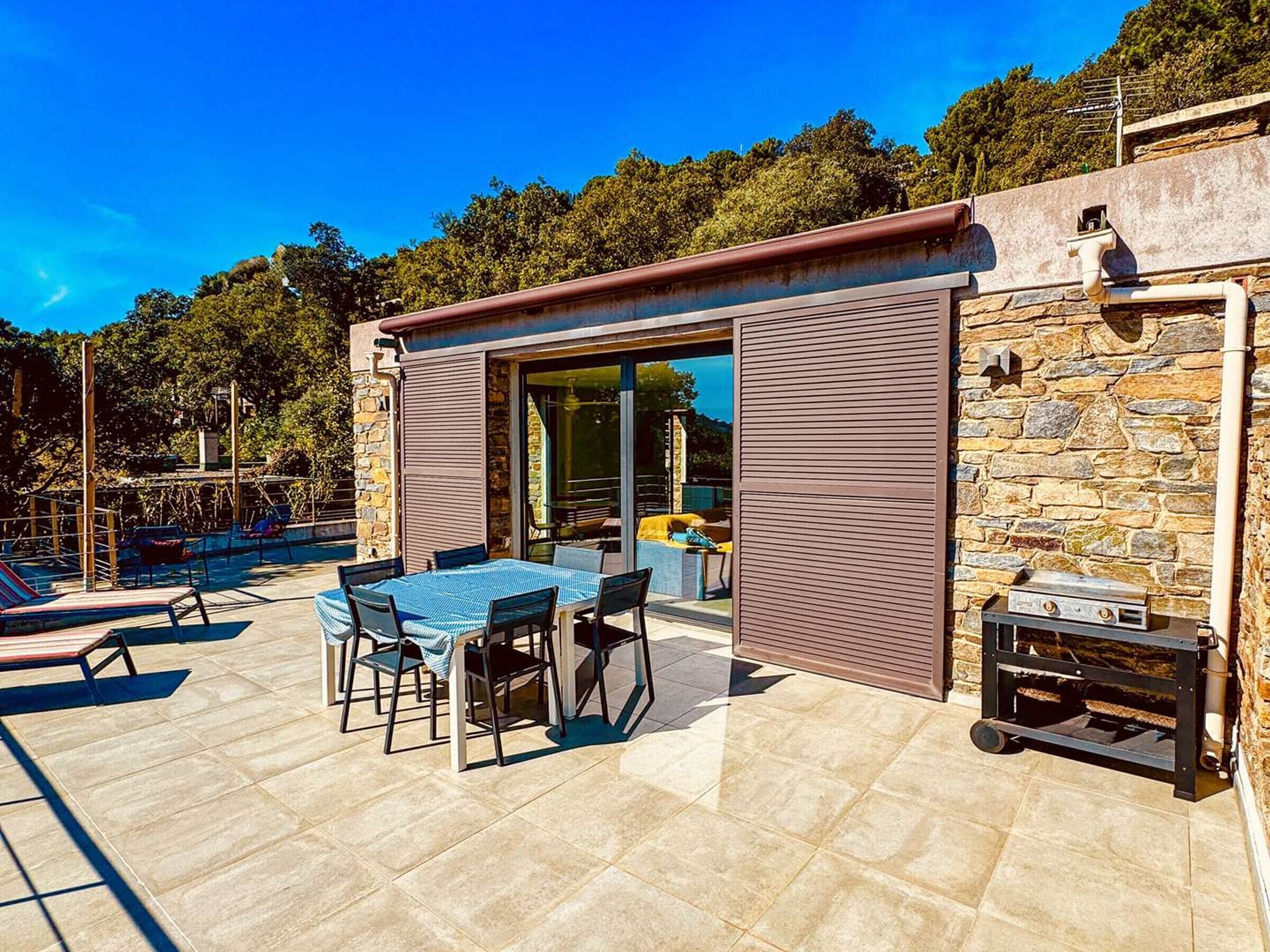 Eine Terrassengruppe im Freien mit Tisch, Stühlen, einem Grill und einer Steinmauer.