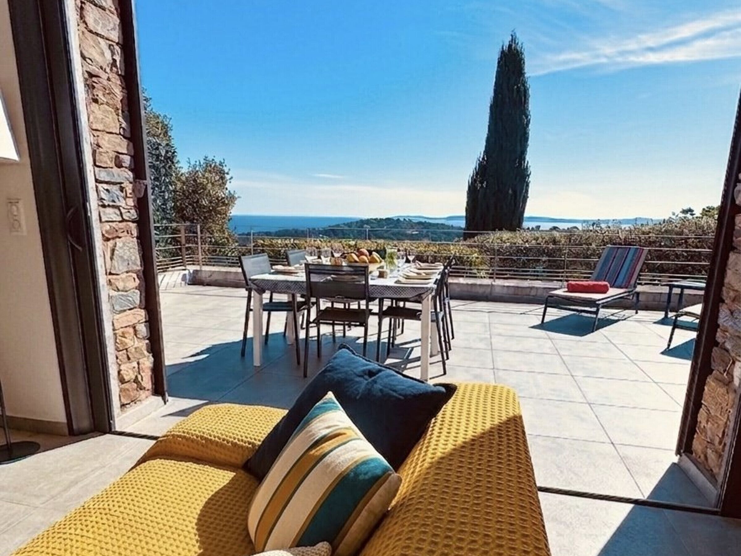 An open terrace with a dining table, chairs, and a sofa with cushions.