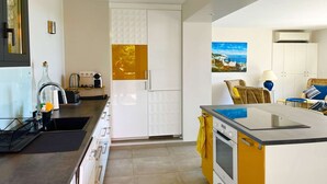 Une cuisine moderne avec des meubles blancs, un plan de travail jaune et un tableau représentant un paysage côtier.