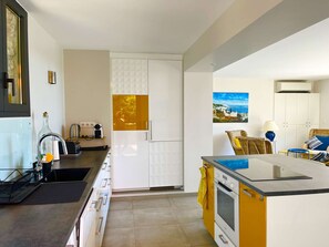 Eine moderne Küche mit weißen Schränken, einer gelben Arbeitsplatte und einem Gemälde von einer Küstenlandschaft.