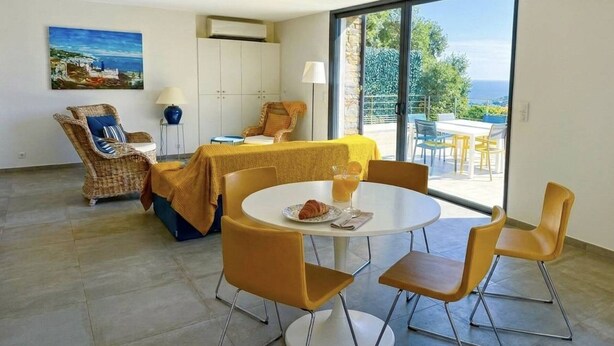 Une pièce comprenant une table à manger, des chaises, un lit, un ventilateur de plafond et une grande fenêtre donnant sur un beau paysage.