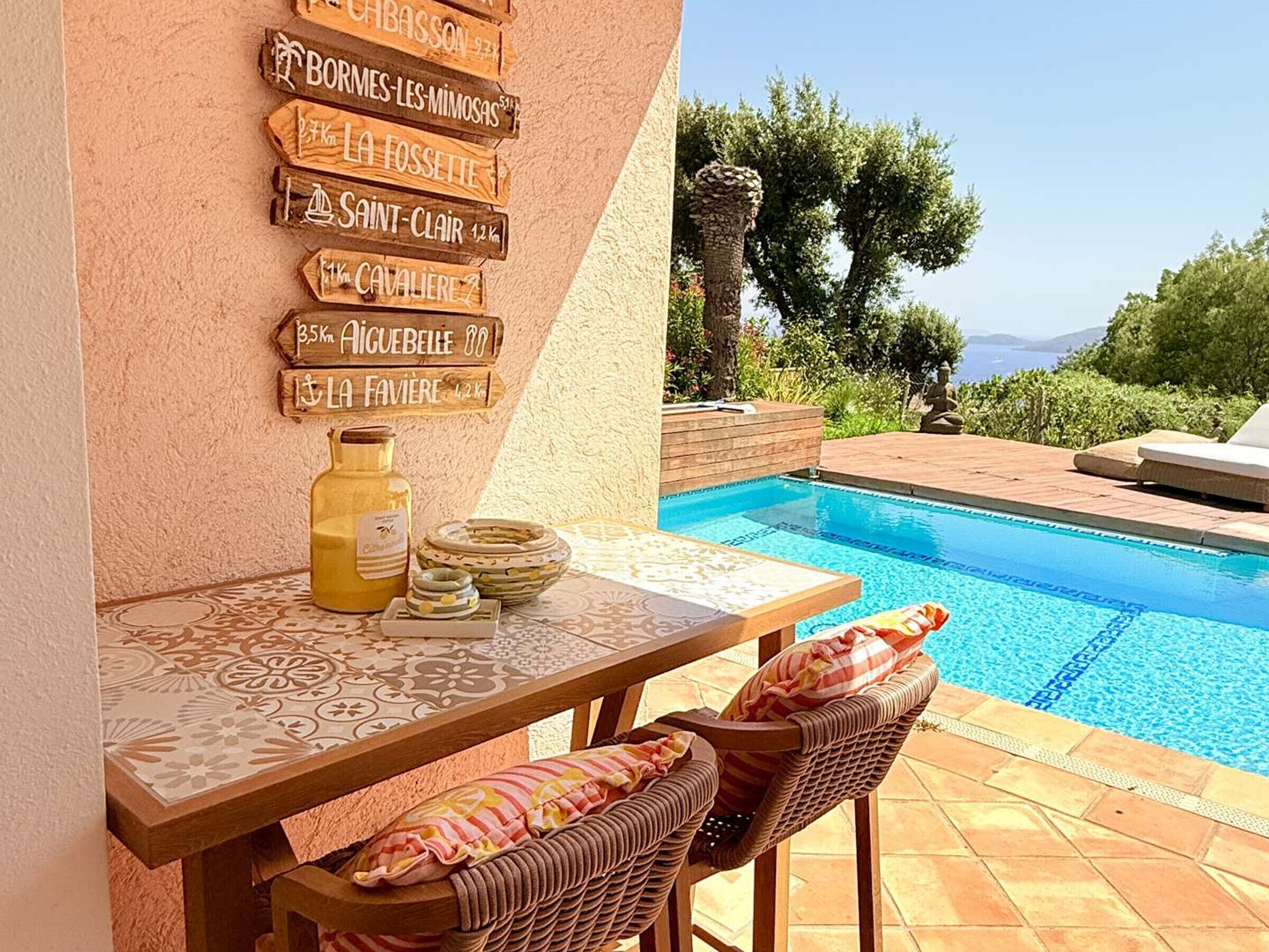 A poolside area with a table, chairs, and a signpost listing distances to various locations.