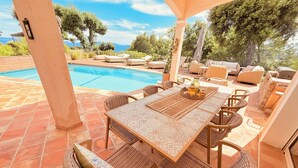 An outdoor patio with a pool, wicker furniture, and a view of the sea. - Villa, sea view, 14 guests (Le Lavandou)