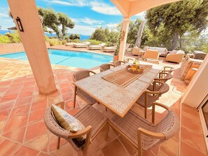 Eine Terrasse im Freien mit Pool, Korbmöbeln und Meerblick.