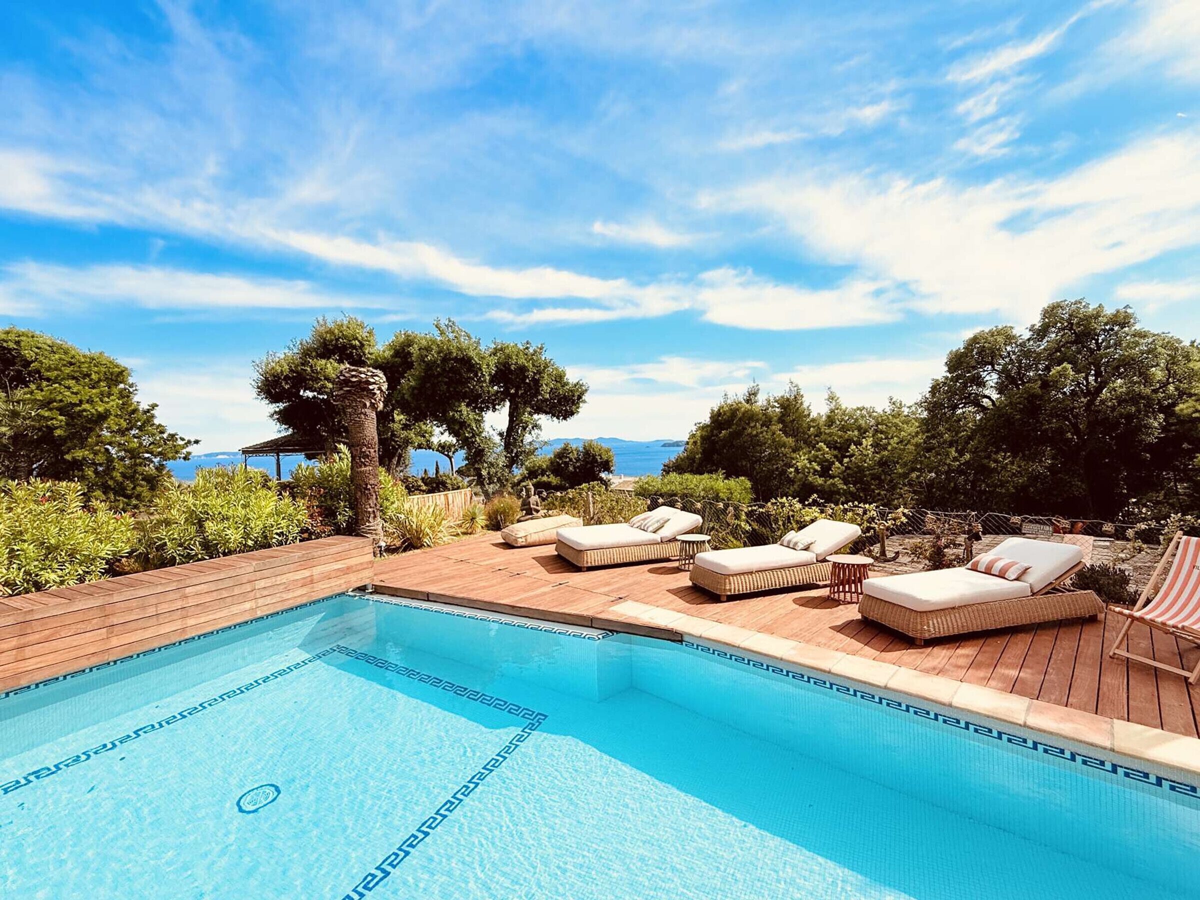 A pool area with lounge chairs and a view of the sea.