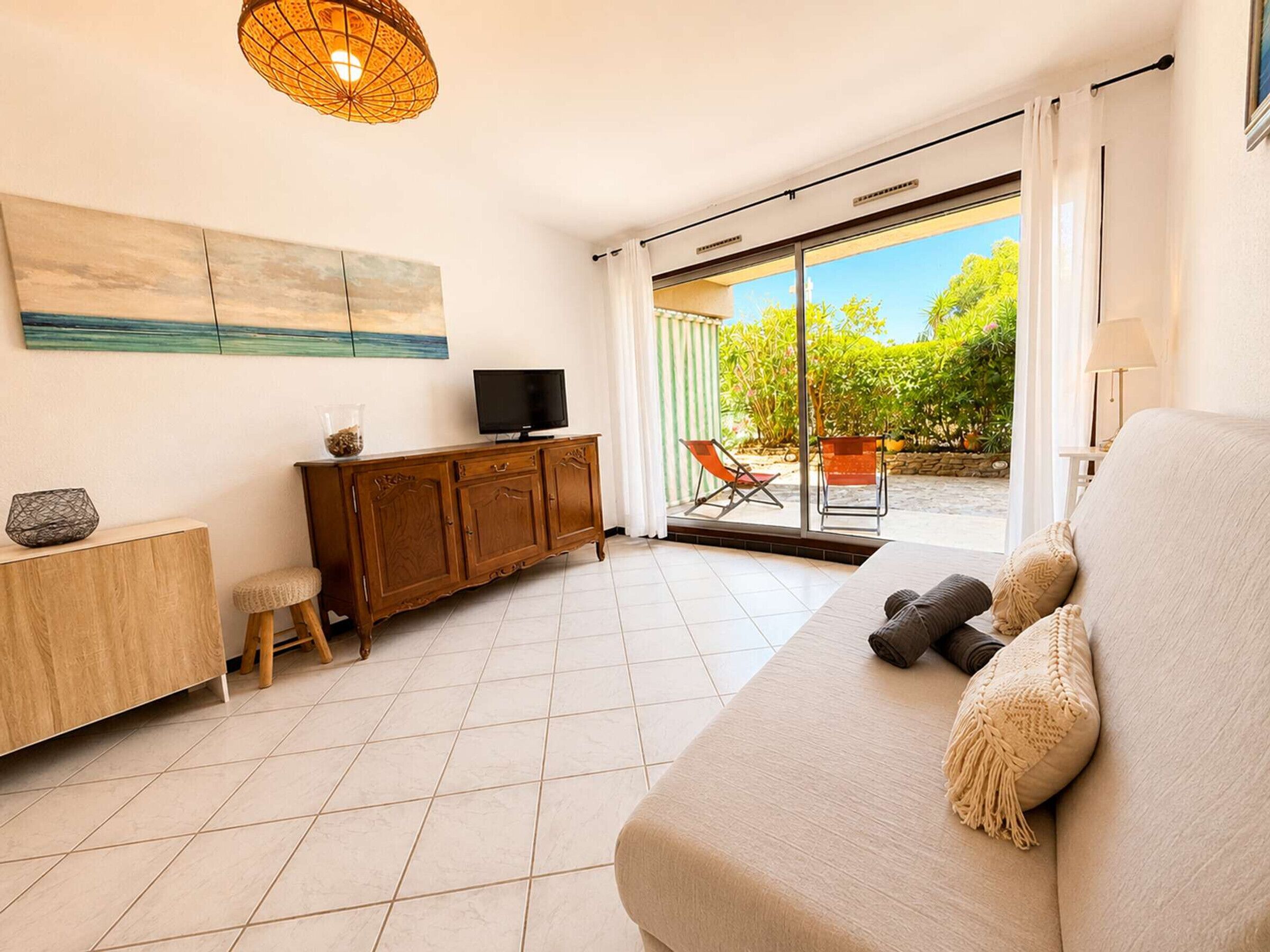 A modern living room with a sofa, a television, a cabinet, and a sliding glass door leading to an outdoor area.