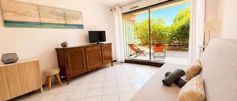 A modern living room with a sofa, a television, a cabinet, and a sliding glass door leading to an outdoor area.