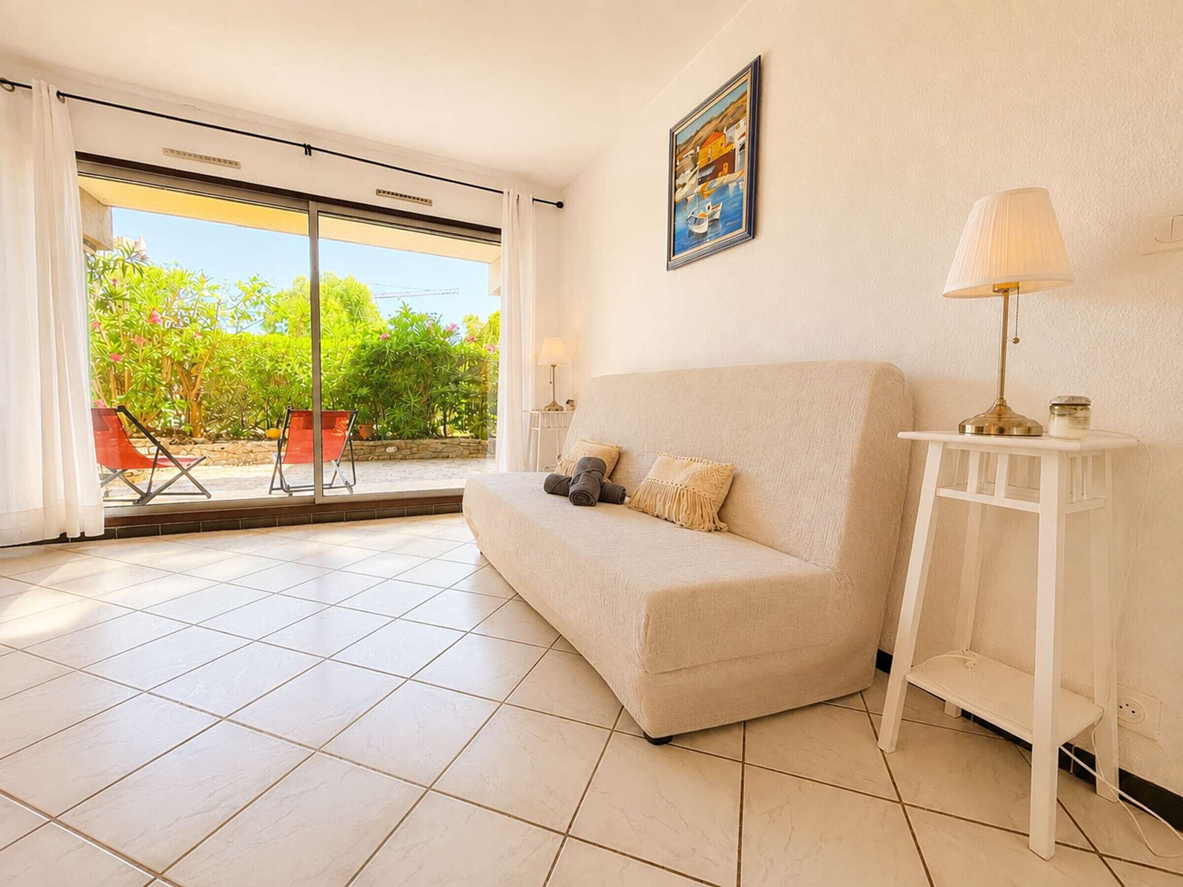 Una sala de estar con un sofá, una lámpara, un cuadro y vistas al exterior con vegetación.