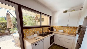 Eine kleine Küche mit Fenster, weißen Schränken, einer Spüle und einem Geschirrspüler.