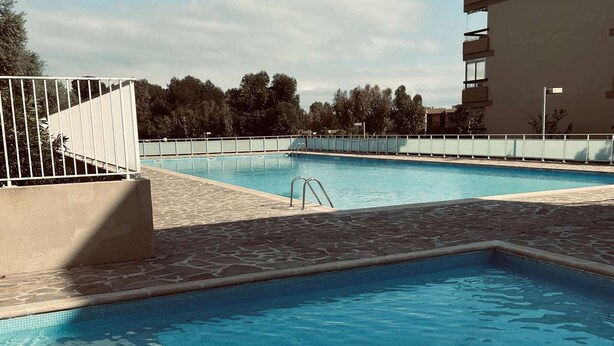 Ein Swimmingpool mit einer Steinterrasse, einer Metallleiter und einem weißen Zaun.