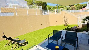 Eine Terrassenanlage im Freien mit einem Glastisch, zwei Stühlen und einer Liege.