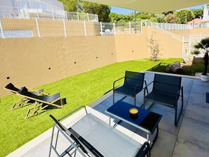 Eine Terrassenanlage im Freien mit einem Glastisch, zwei Stühlen und einer Liege.