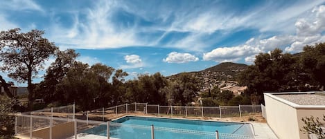 A rectangular swimming pool with a white fence, surrounded by trees and hills in the background.