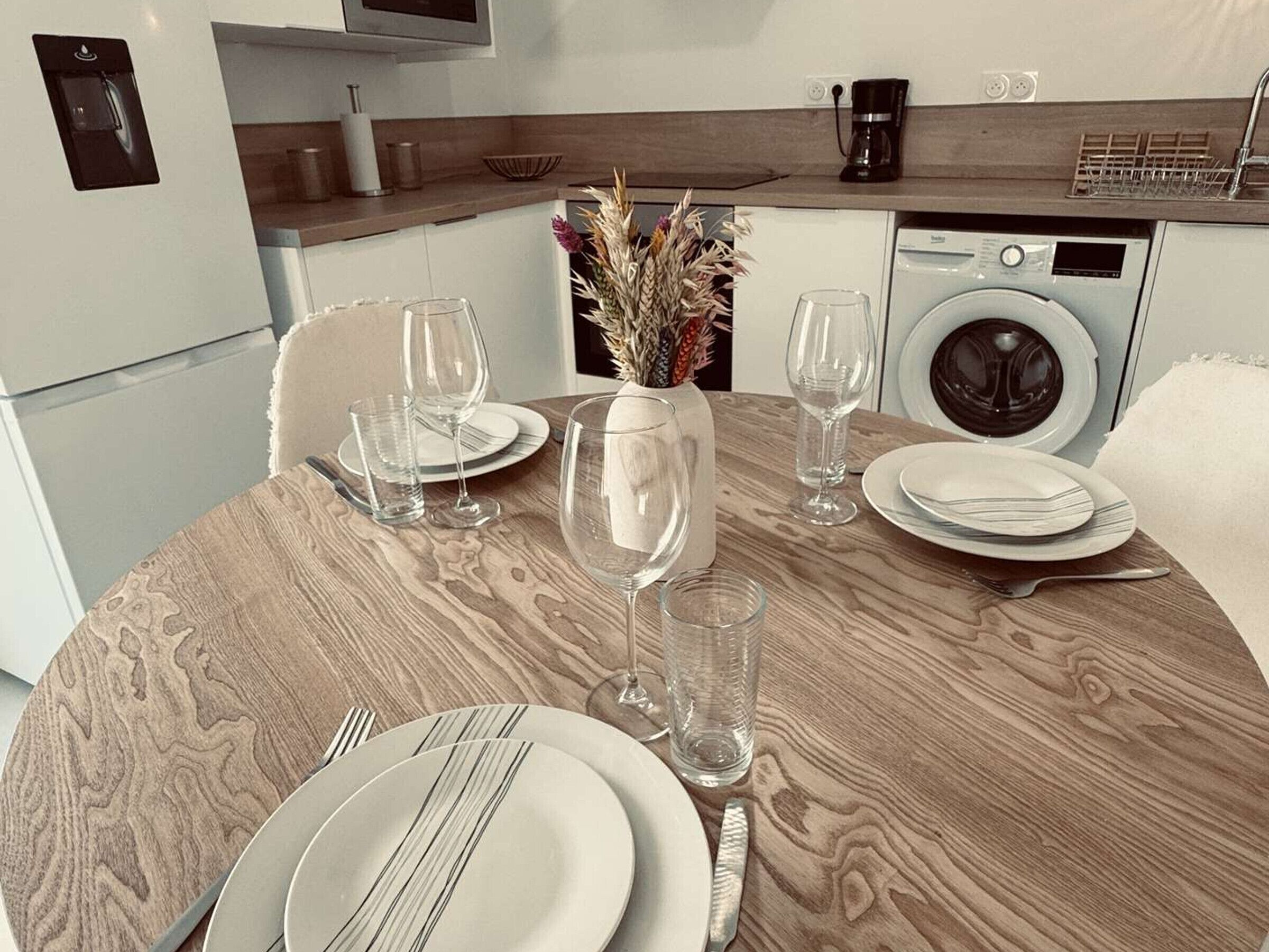 A dining area with a round wooden table set for two, equipped with plates, glasses, and cutlery.