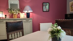 Et spiseområde med et bord dækket til to personer, en blomstervase, en lampe og et indrammet billede på væggen.