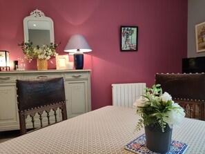 A dining area with a table set for two, a vase of flowers, a lamp, and a framed picture on the wall. - Central T2 with garden, ideal - ? guests (La Roche-Posay)