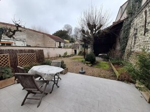 A patio area with a table and chairs, surrounded by a garden with a stone wall and a wooden fence.