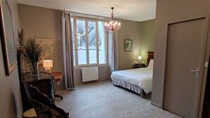 Et hotelværelse med en seng, et skrivebord med lampe, en stol, et vindue med gardiner og en lysekrone.